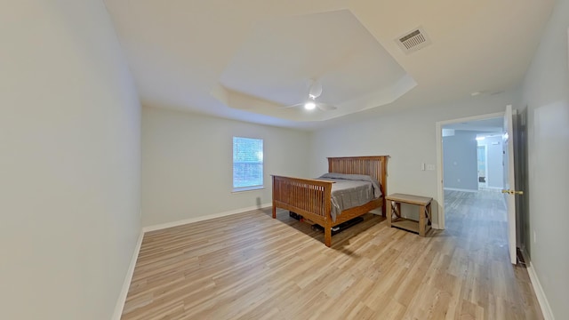 bedroom with ceiling fan, a tray ceiling, and light hardwood / wood-style flooring