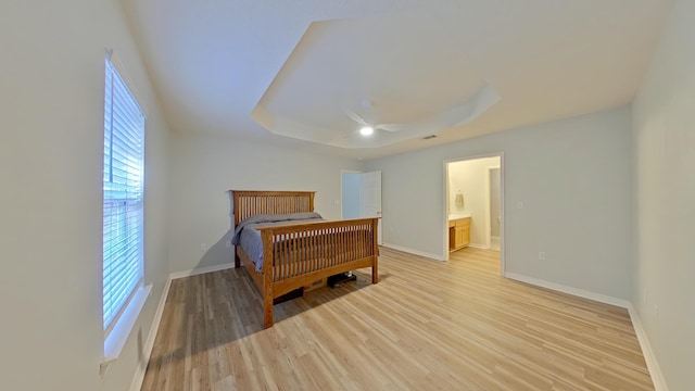 bedroom featuring ceiling fan, ensuite bathroom, a raised ceiling, and light hardwood / wood-style flooring