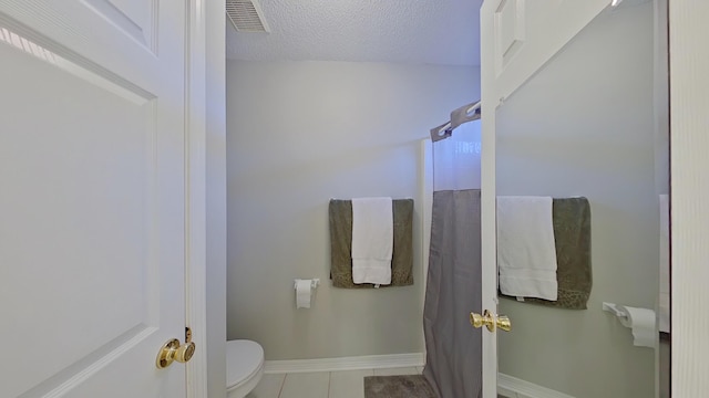 bathroom with a textured ceiling, toilet, and tile patterned flooring