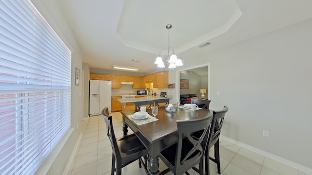 dining room featuring light tile patterned flooring, an inviting chandelier, and a tray ceiling