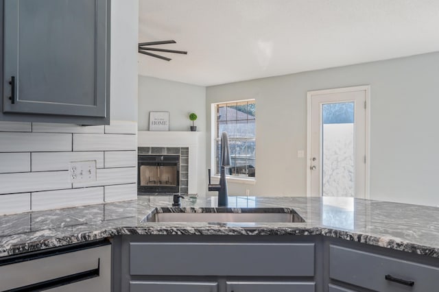 kitchen with dark stone countertops, tasteful backsplash, sink, a fireplace, and gray cabinets