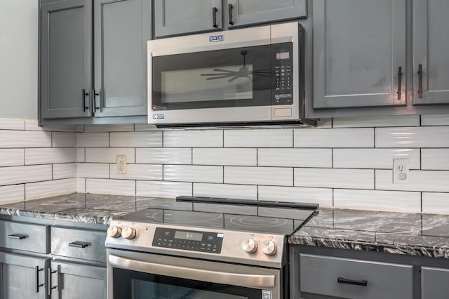 kitchen with appliances with stainless steel finishes, gray cabinetry, and dark stone counters