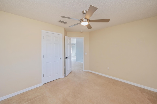 spare room featuring light carpet, ceiling fan, and a textured ceiling