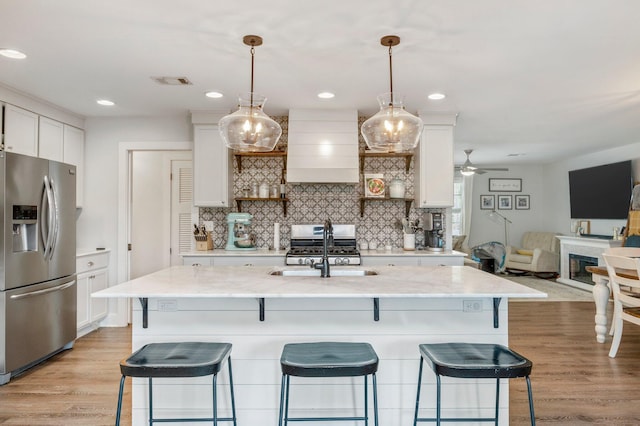 kitchen with wall chimney range hood, stainless steel fridge with ice dispenser, hanging light fixtures, and white cabinets