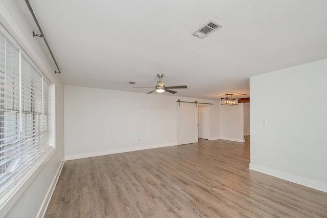 spare room featuring ceiling fan, a barn door, and hardwood / wood-style floors