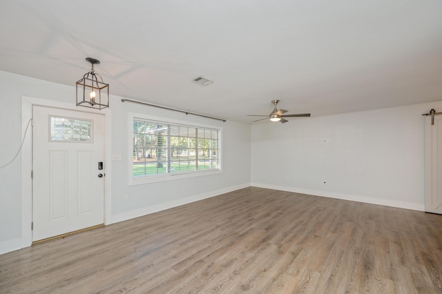 foyer entrance with ceiling fan with notable chandelier, light hardwood / wood-style flooring, and a barn door