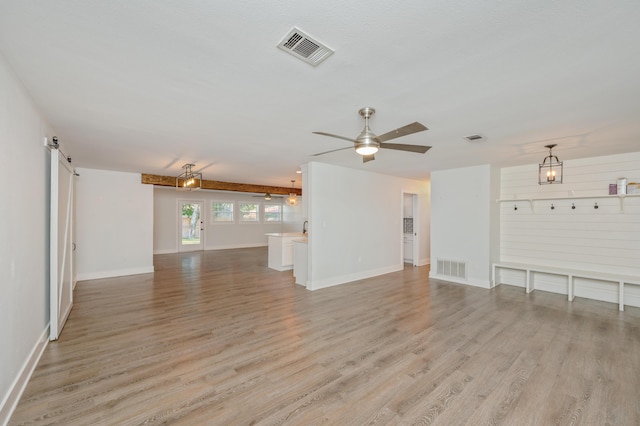 unfurnished living room featuring ceiling fan, a barn door, and light hardwood / wood-style floors