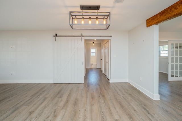 unfurnished room featuring beamed ceiling, a barn door, and light hardwood / wood-style flooring