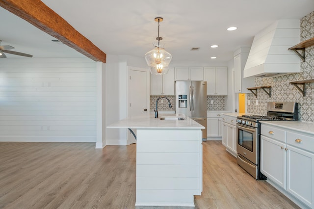 kitchen with sink, premium range hood, appliances with stainless steel finishes, hanging light fixtures, and an island with sink