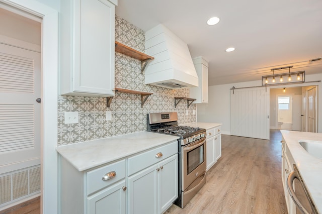 kitchen featuring white cabinetry, stainless steel appliances, a barn door, and custom range hood