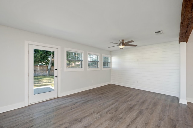 empty room with plenty of natural light, dark wood-type flooring, ceiling fan, and wood walls