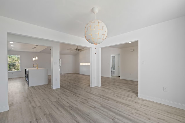 empty room featuring ceiling fan with notable chandelier, lofted ceiling, light hardwood / wood-style floors, and sink