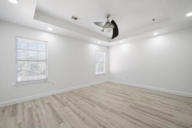 unfurnished room featuring a raised ceiling, ceiling fan, a wealth of natural light, and light hardwood / wood-style floors