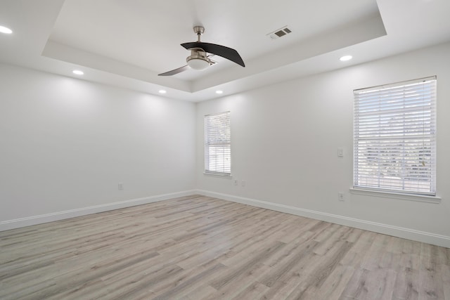 unfurnished room featuring light hardwood / wood-style floors, plenty of natural light, a raised ceiling, and ceiling fan