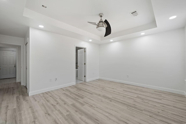 spare room with ceiling fan, light hardwood / wood-style floors, and a raised ceiling