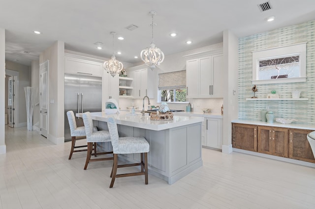 kitchen featuring open shelves, light countertops, visible vents, stainless steel built in fridge, and an island with sink