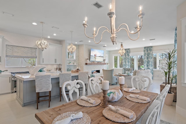 dining space featuring visible vents, a lit fireplace, light wood-style floors, a chandelier, and recessed lighting