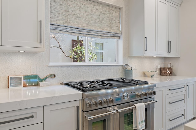 kitchen with light stone countertops, double oven range, backsplash, and white cabinetry