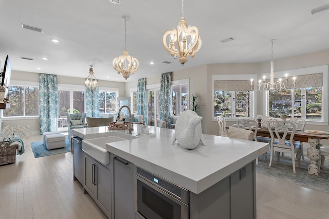 kitchen featuring light wood-style flooring, a notable chandelier, a sink, gray cabinets, and stainless steel microwave