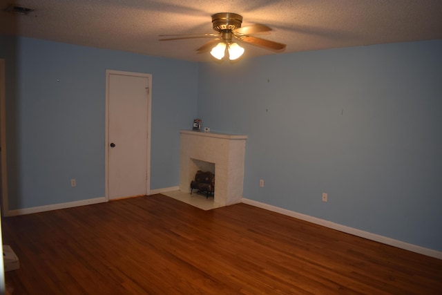 unfurnished living room featuring ceiling fan, a brick fireplace, a textured ceiling, and dark hardwood / wood-style flooring