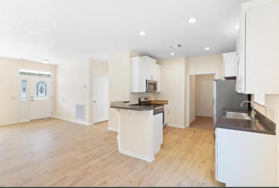 kitchen with white cabinetry, sink, a kitchen breakfast bar, kitchen peninsula, and light wood-type flooring