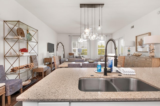 kitchen with hanging light fixtures, light stone countertops, sink, and hardwood / wood-style floors