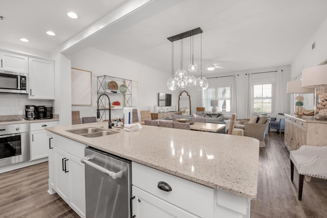 kitchen featuring appliances with stainless steel finishes, decorative light fixtures, sink, white cabinets, and a center island with sink