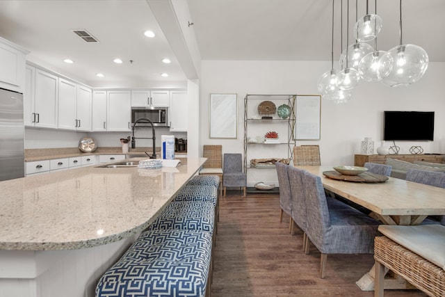 kitchen featuring sink, light stone counters, hanging light fixtures, dark hardwood / wood-style floors, and white cabinets