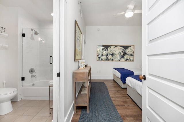 bathroom with ceiling fan, hardwood / wood-style floors, shower / bath combination with glass door, and toilet