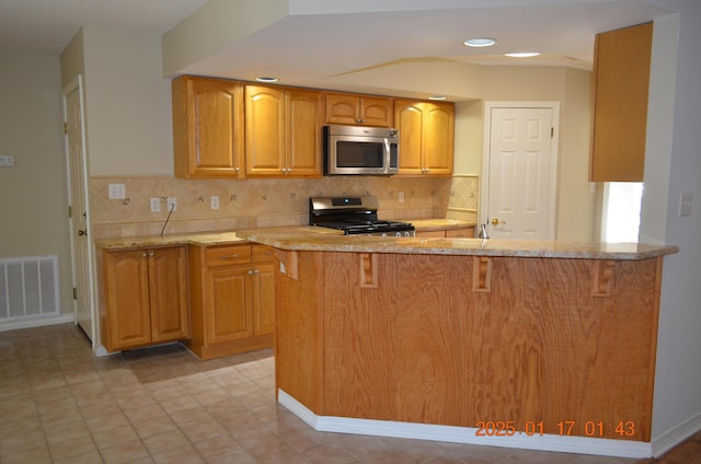 kitchen with light stone counters, backsplash, kitchen peninsula, and appliances with stainless steel finishes