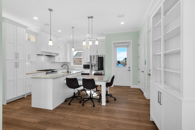 kitchen featuring pendant lighting, an island with sink, white cabinetry, light stone counters, and stainless steel appliances