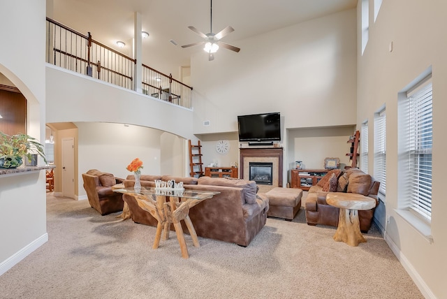 living room featuring ceiling fan, light colored carpet, and a high ceiling