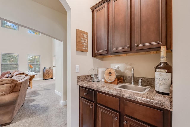 bar featuring light colored carpet, sink, and dark stone countertops