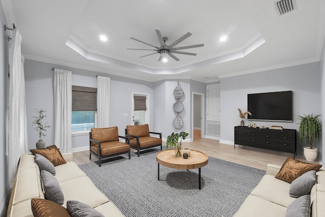 living room with a raised ceiling, light wood-type flooring, ornamental molding, and ceiling fan