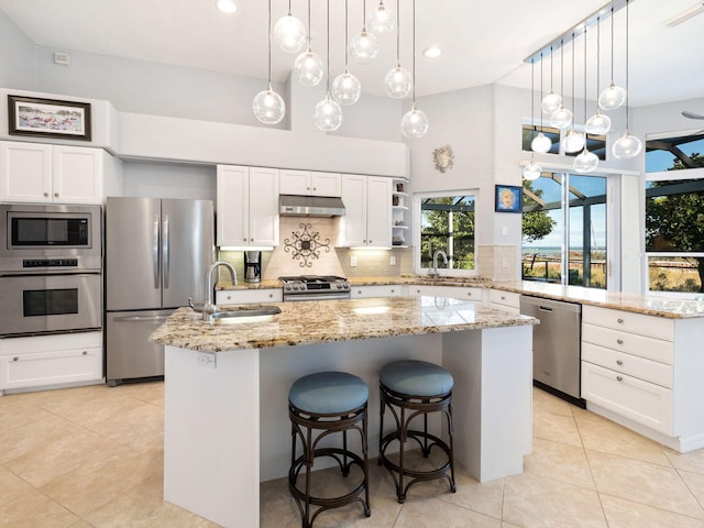 kitchen with sink, appliances with stainless steel finishes, pendant lighting, a kitchen island with sink, and backsplash