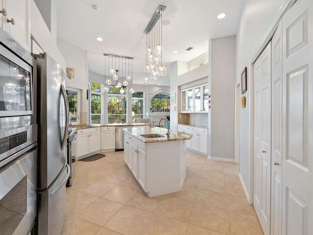 kitchen featuring sink, stainless steel appliances, light stone counters, an island with sink, and decorative backsplash