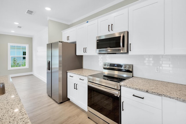 kitchen with light stone countertops, ornamental molding, white cabinets, and appliances with stainless steel finishes