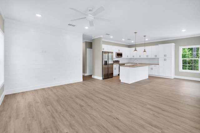 kitchen with sink, a center island with sink, pendant lighting, stainless steel appliances, and white cabinets