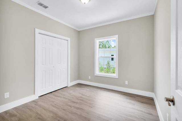 unfurnished bedroom featuring crown molding, light hardwood / wood-style flooring, and a closet