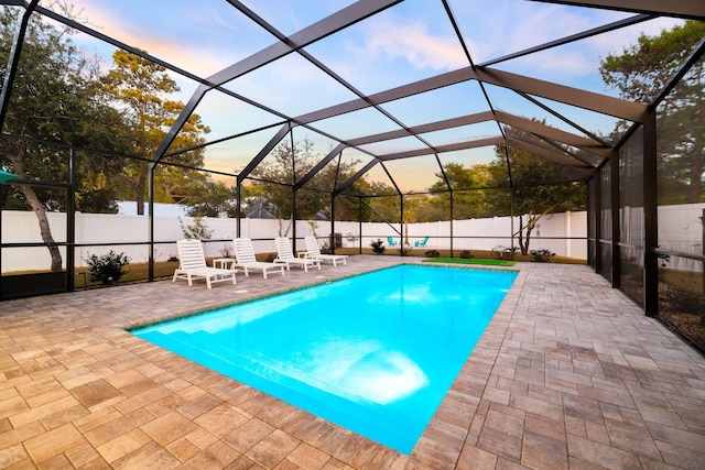 pool at dusk featuring a lanai and a patio