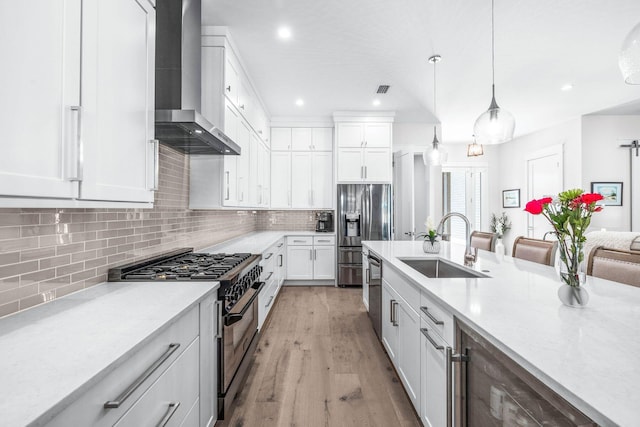 kitchen with decorative light fixtures, sink, appliances with stainless steel finishes, white cabinets, and wall chimney exhaust hood