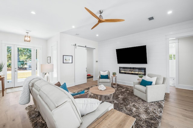 living room with ceiling fan, a barn door, a large fireplace, and light hardwood / wood-style flooring