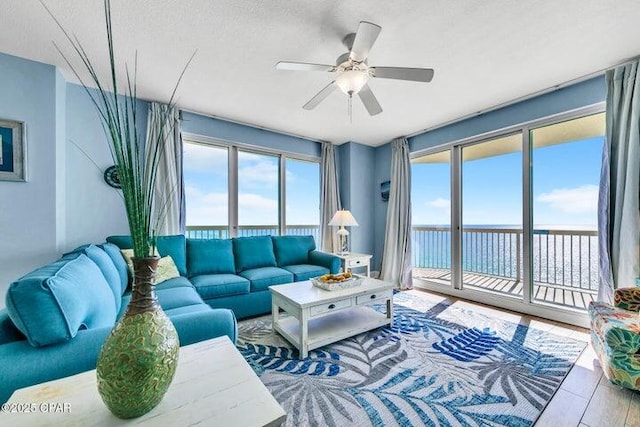 living room featuring a textured ceiling, ceiling fan, a water view, and hardwood / wood-style floors