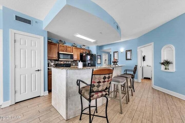 14825 Front Beach Rd Unit 2001, Panama City Beach, FL 32413 - kitchen featuring light wood-type flooring, a kitchen island with sink, black fridge with ice dispenser, and a breakfast bar area