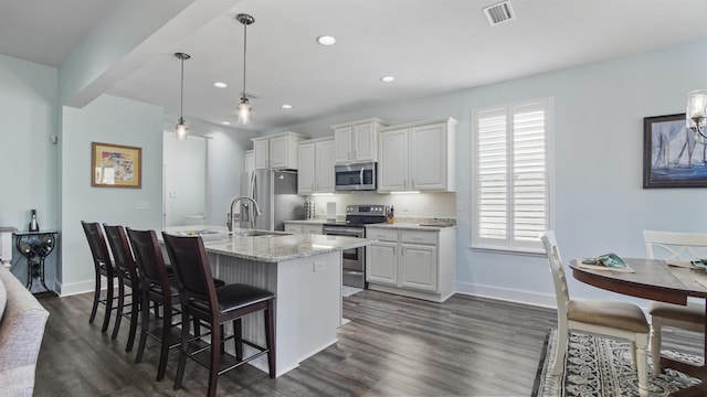 kitchen featuring hanging light fixtures, stainless steel appliances, light stone countertops, an island with sink, and white cabinets