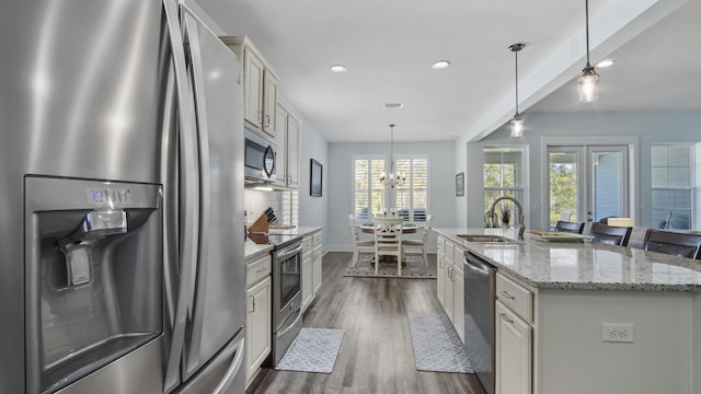 kitchen featuring sink, hanging light fixtures, a kitchen island with sink, stainless steel appliances, and light stone countertops