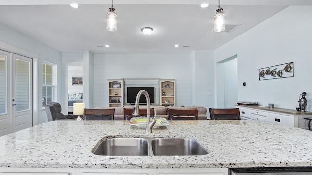 kitchen featuring pendant lighting, sink, a kitchen island with sink, and light stone counters