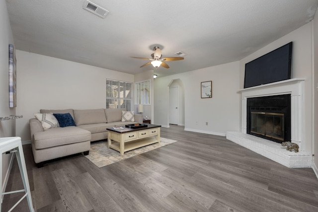 living area with ceiling fan, a fireplace, wood finished floors, visible vents, and baseboards