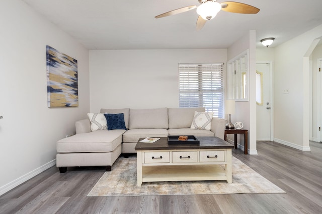 living room featuring a ceiling fan, arched walkways, baseboards, and wood finished floors