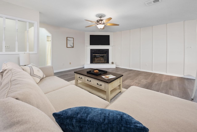 living area featuring ceiling fan, wood finished floors, visible vents, baseboards, and a glass covered fireplace